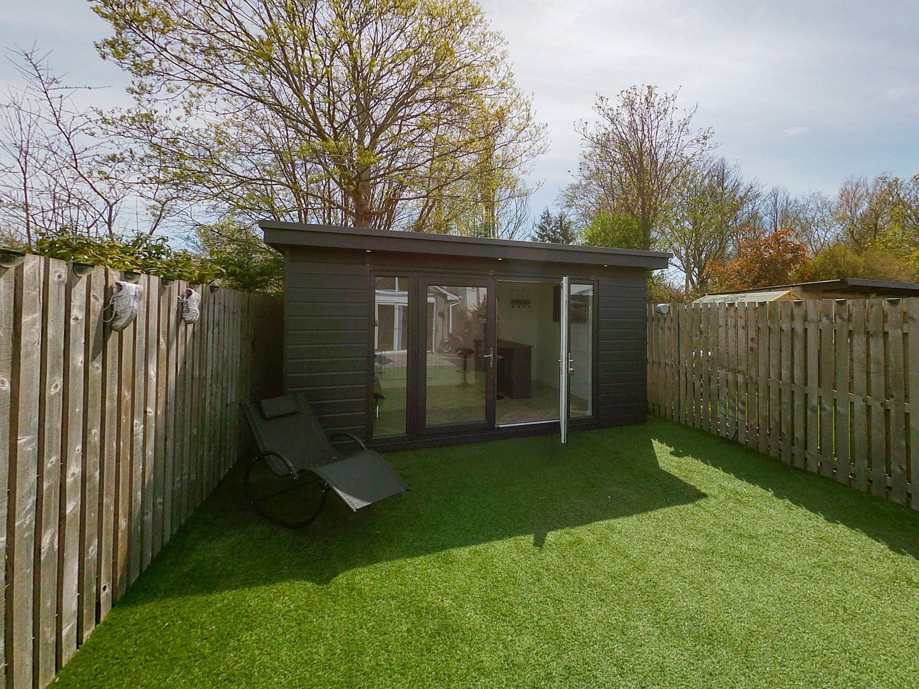 Dark-clad garden building with glazed doors at the end of a lawned garden