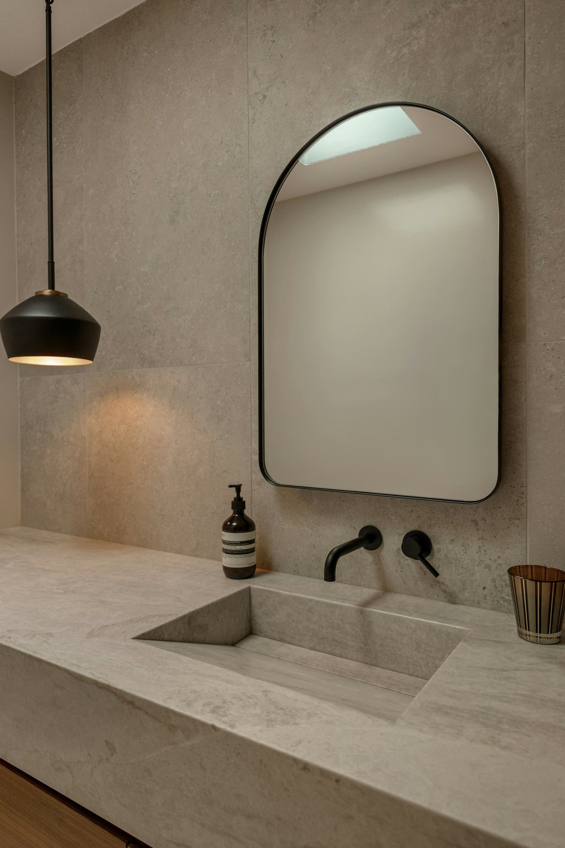 Stone vanity with an arched mirror and black pendant light