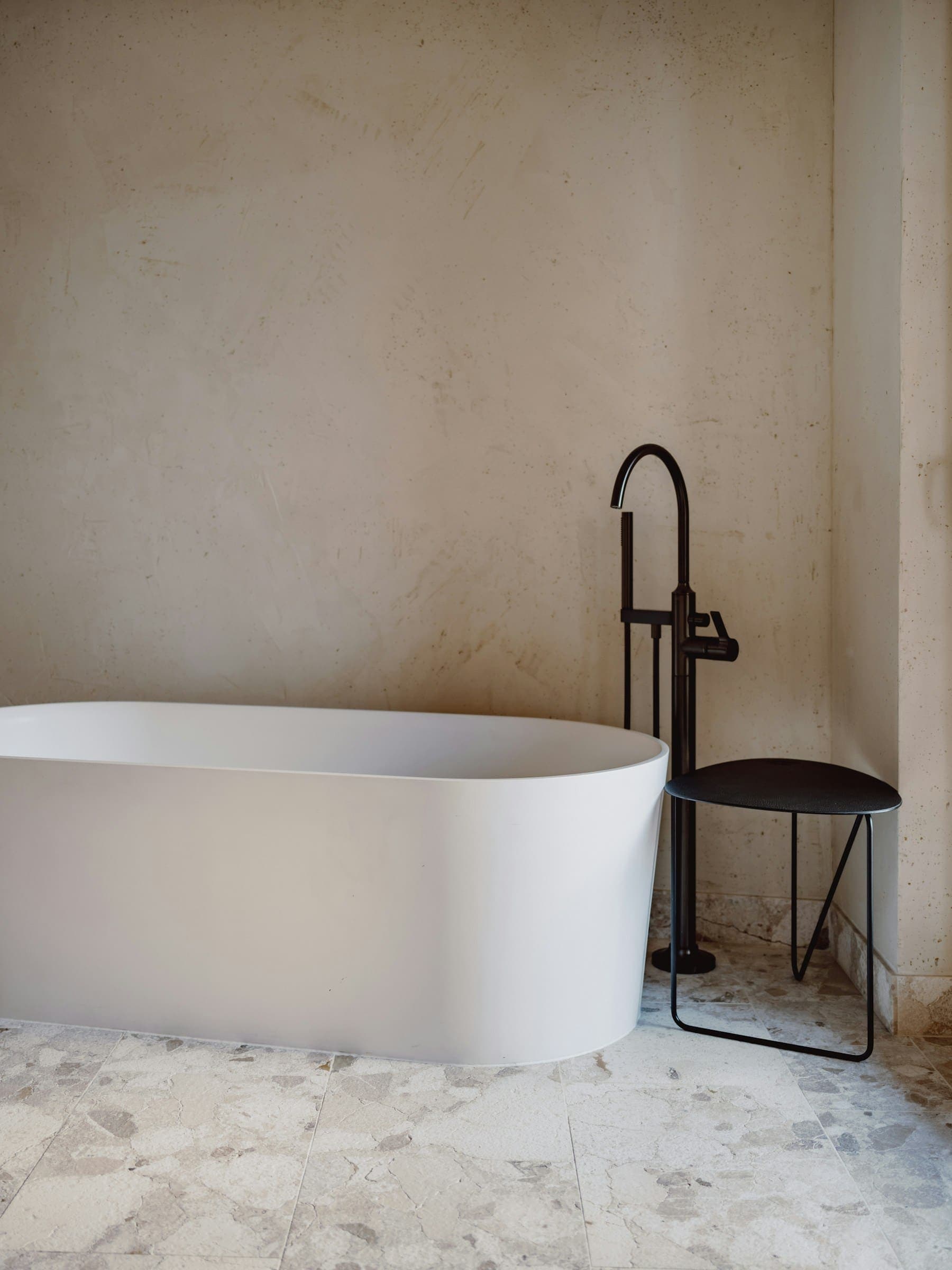 Black floor-standing bath filler beside a white freestanding bath