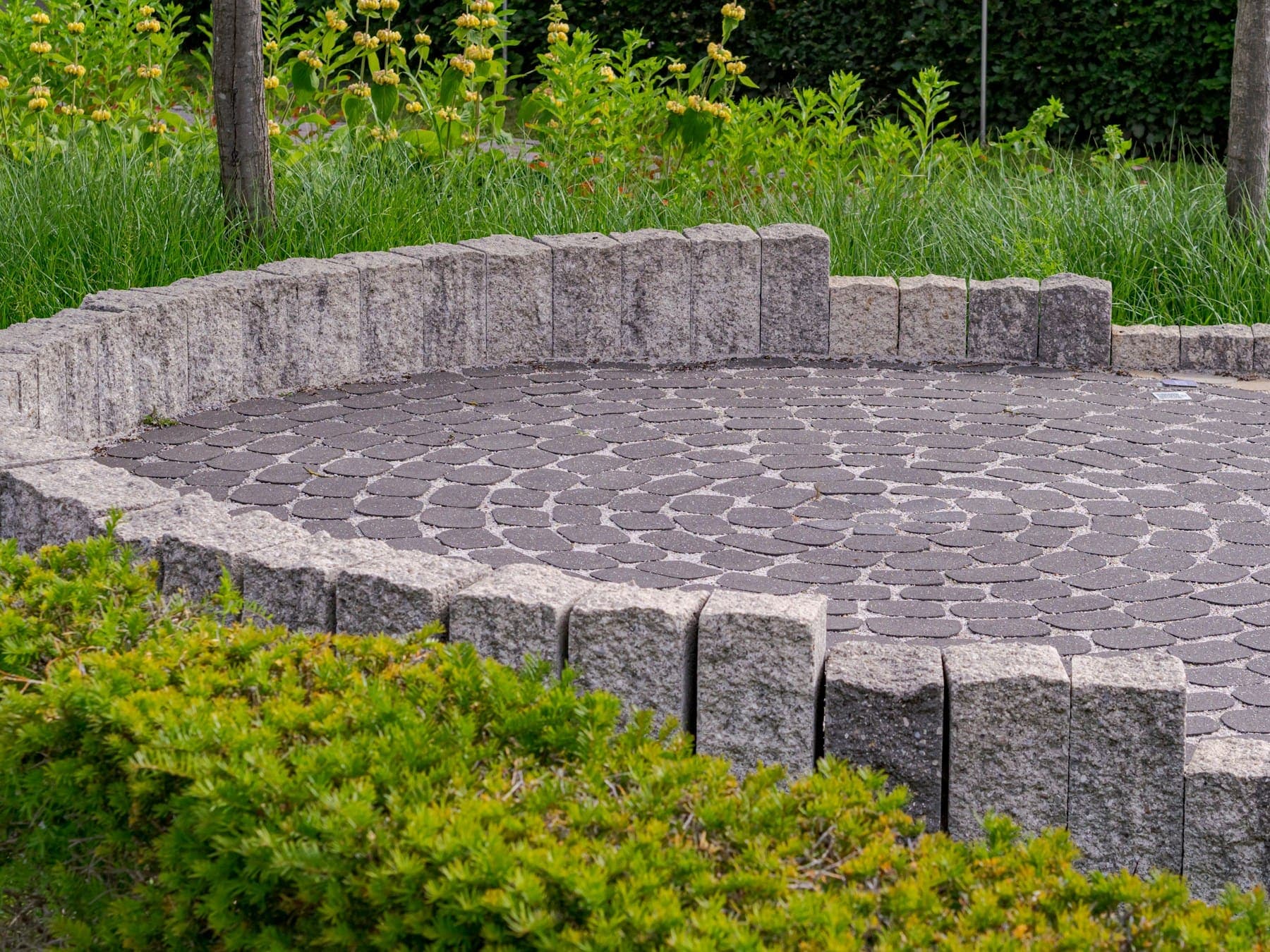 Circular granite-sett patio edged with upright stone and low planting