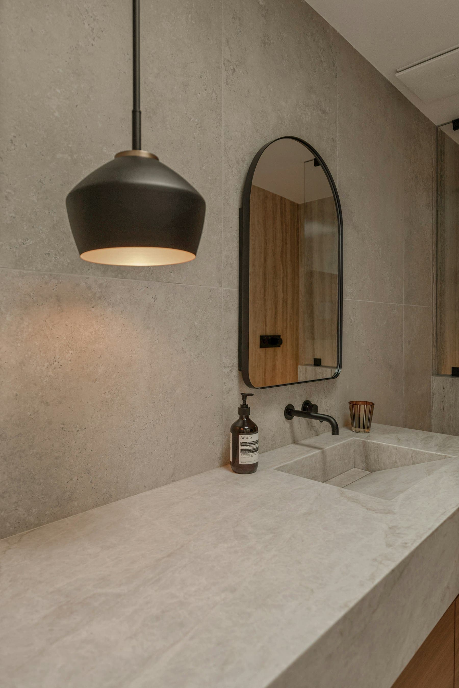 Stone vanity with arched mirror lit by a black pendant