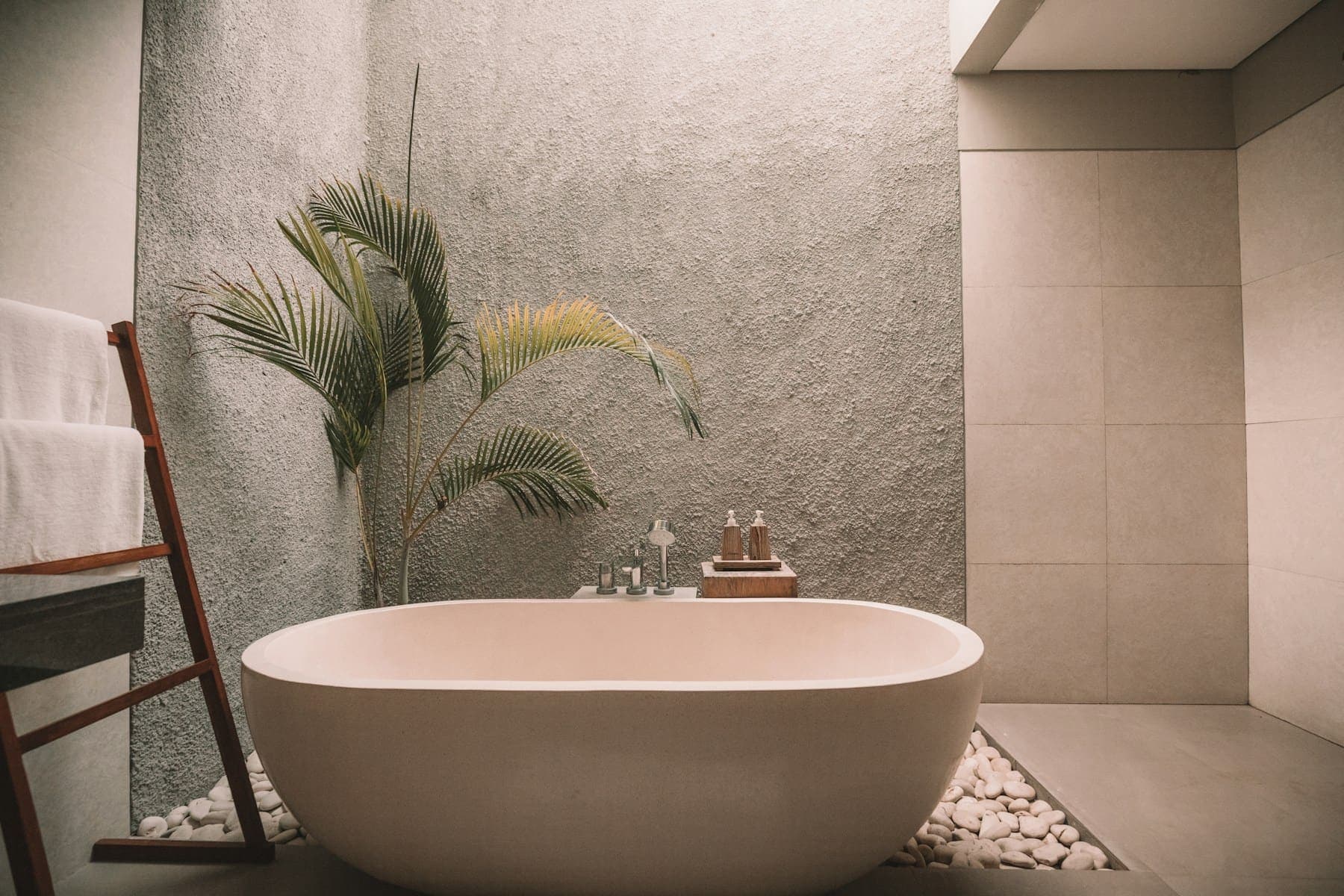 Oval freestanding bath in front of a textured stone wall with a tall plant