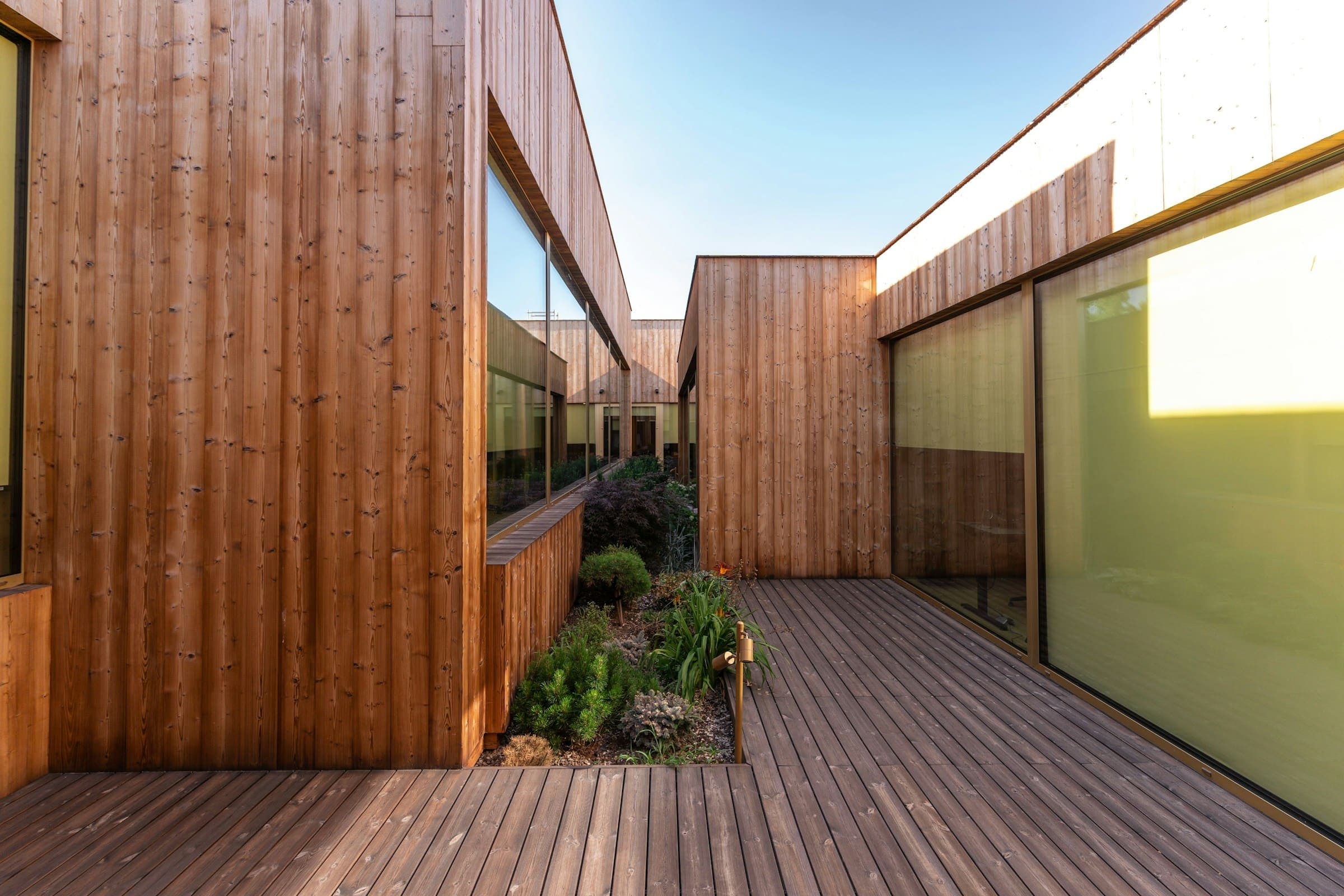 Timber-clad buildings with large glazed walls around a decked courtyard