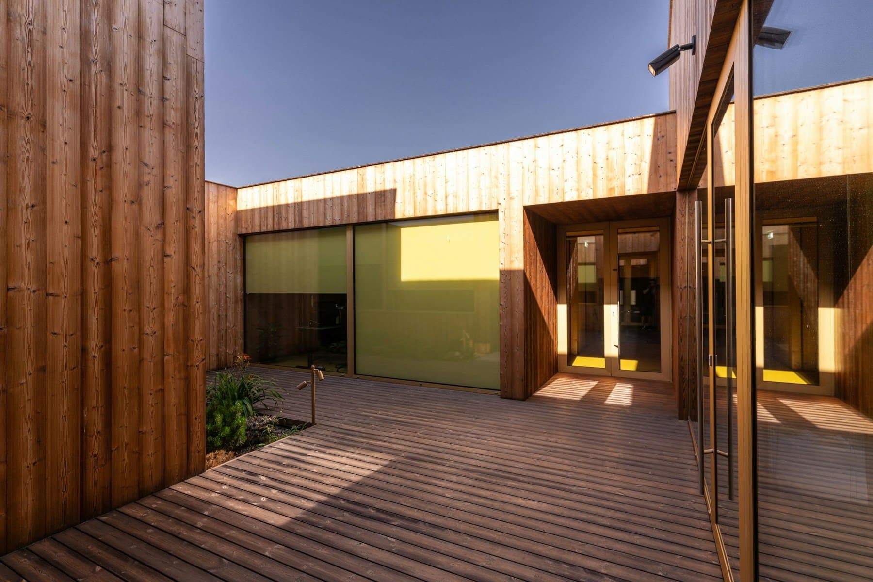 Glazed entrance to a timber-clad building at the end of a decked walkway