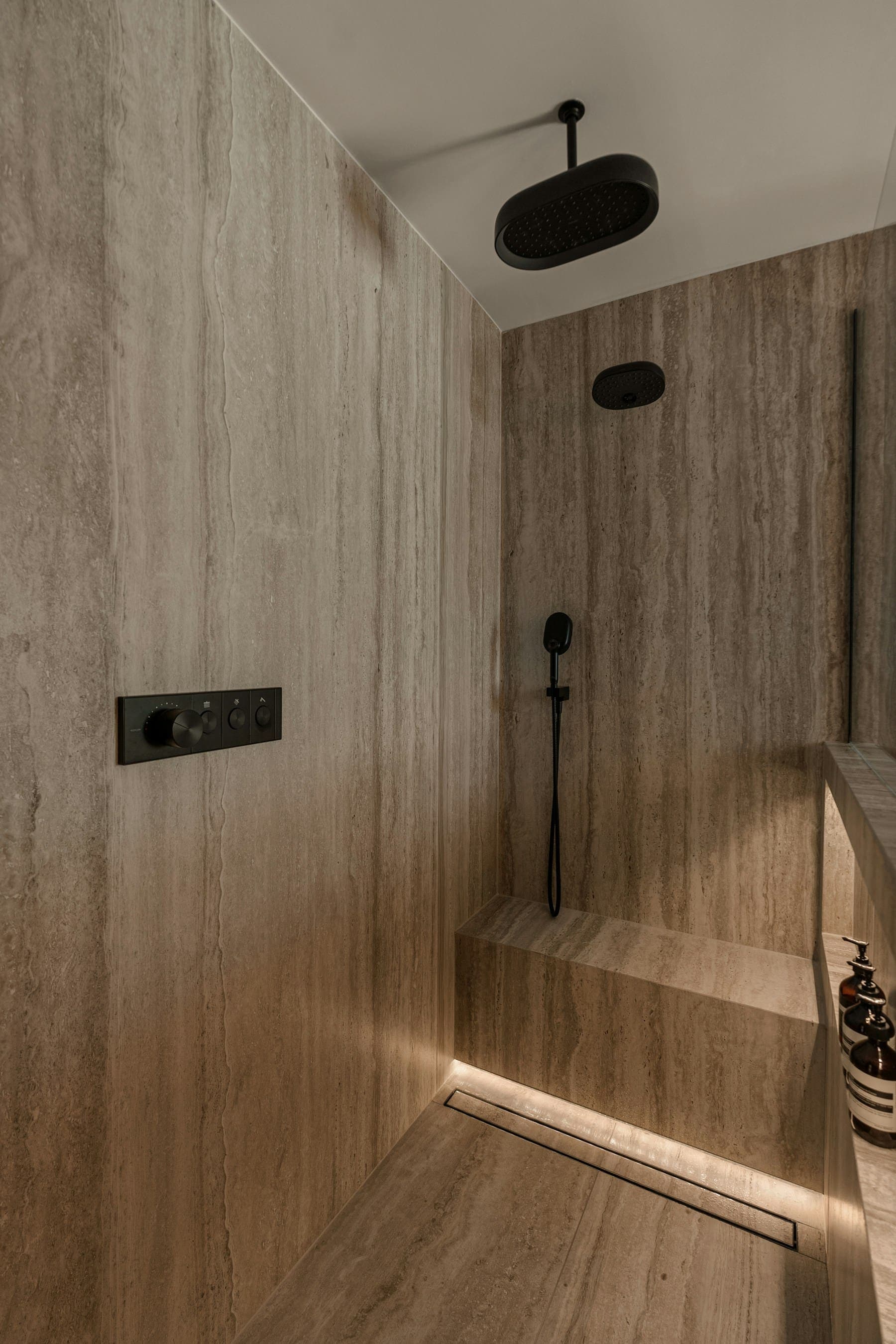 Walk-in shower lined with travertine stone and matt black controls
